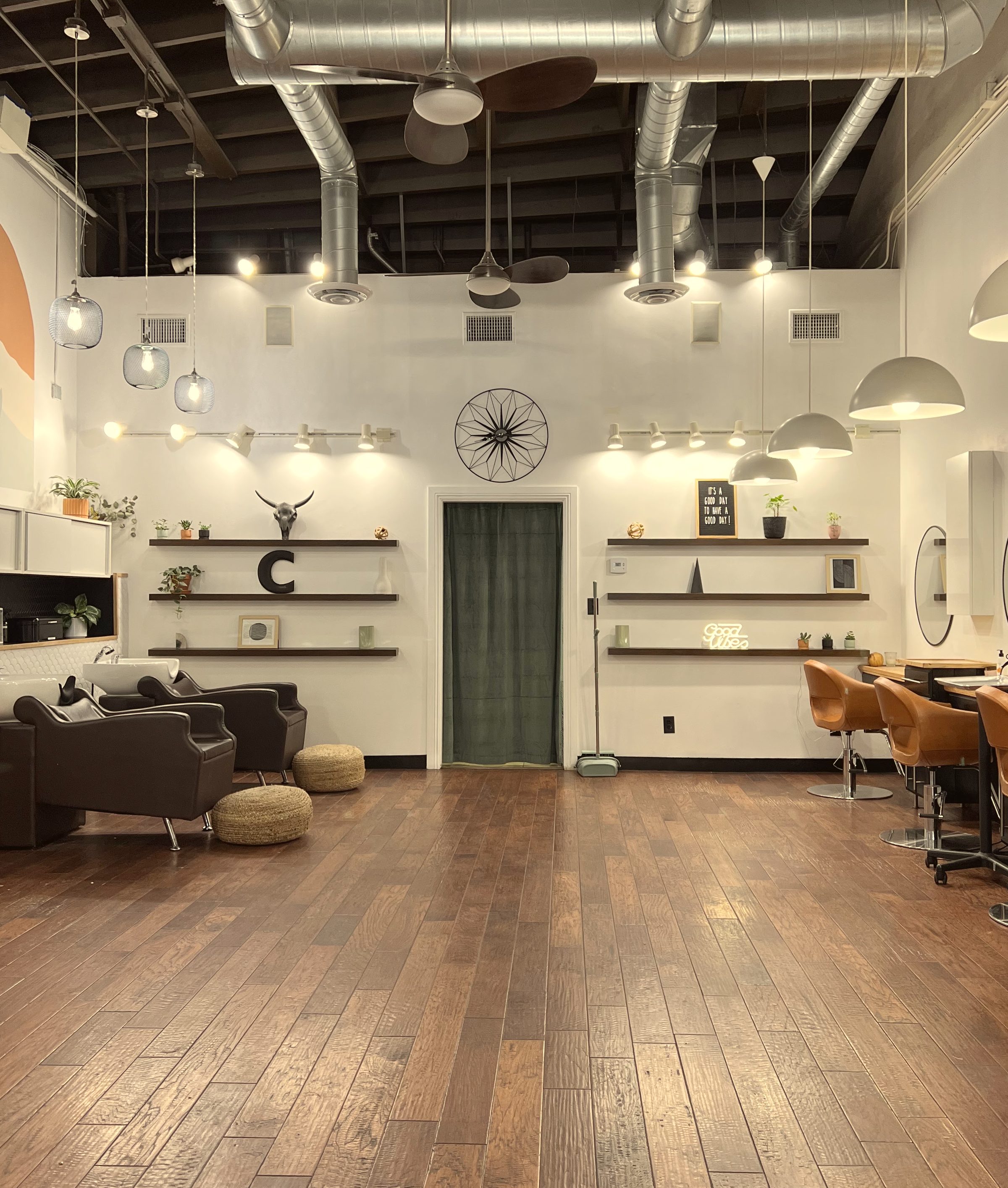 Inside Salon Celeste through the front door: the dark wood floor, the cognac leather chairs, the shelves with a steer skull, a big black C, the letterboard and a Good vibes neon